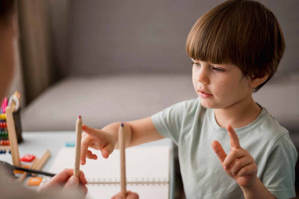 Un jeune enfant assis à une table chez lui, apprenant à compter avec des crayons de couleur, illustrant le développement cognitif précoce et la concentration.