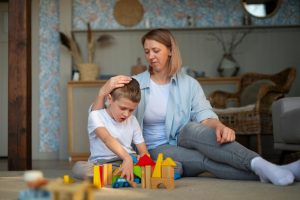 Une mère est assise par terre et joue avec son fils autiste, utilisant des jouets colorés pour favoriser le lien et l'apprentissage.