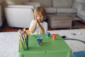 Enfant assis à une table verte, dessinant calmement avec des crayons de couleur et concentré sur une activité artistique.