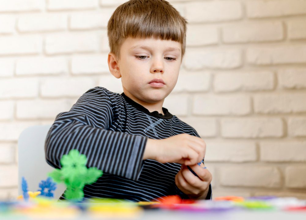 Jeune enfant assis à une table, concentré sur la manipulation de petites pièces de construction colorées, illustrant l’attention.