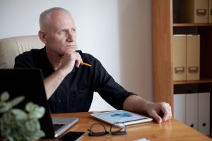 Homme d’âge moyen assis à son bureau, réfléchissant avec un crayon, illustrant les difficultés d’attention et de concentration chez l’adulte avec TDAH.