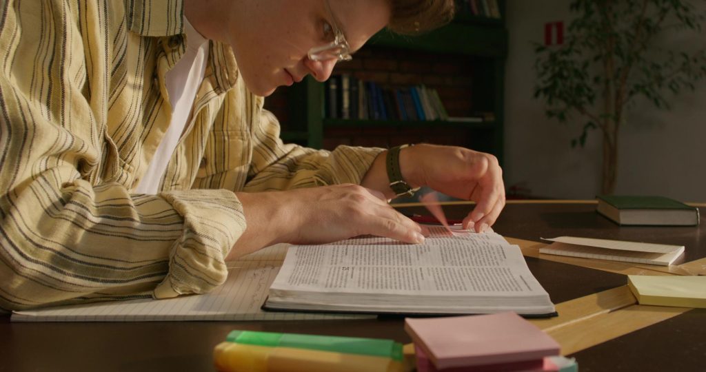 Un homme adulte suit les lignes d'un texte du doigt, concentré sur sa lecture.