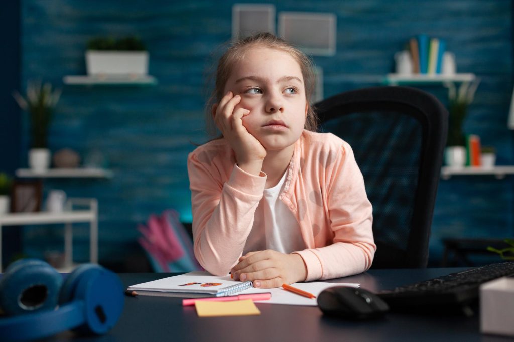 Fillette distraite à son bureau, un signe d'attention associé au TDAH ou au TSA.