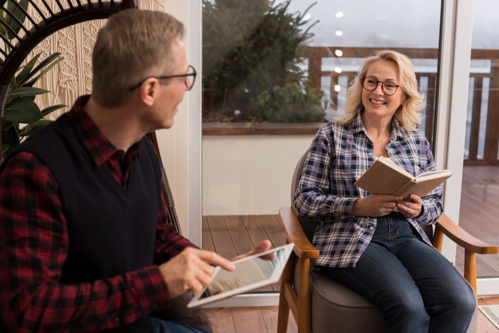 Femme souriante, livre en main, en discussion avec un homme tenant une tablette : un échange évoquant la remise des résultats d'évaluation.