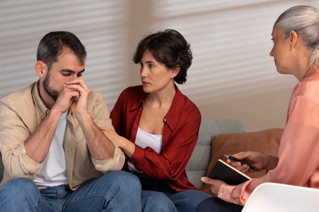 Un homme, soutenu par sa conjointe, pendant qu'une intervenante prend des notes lors d'une rencontre d'évaluation neuropsychologique.