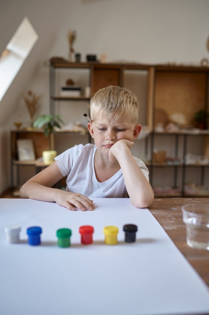Garçon fixe des pots de peinture colorés, illustrant des différences d'attention liées au TDAH ou au TSA.