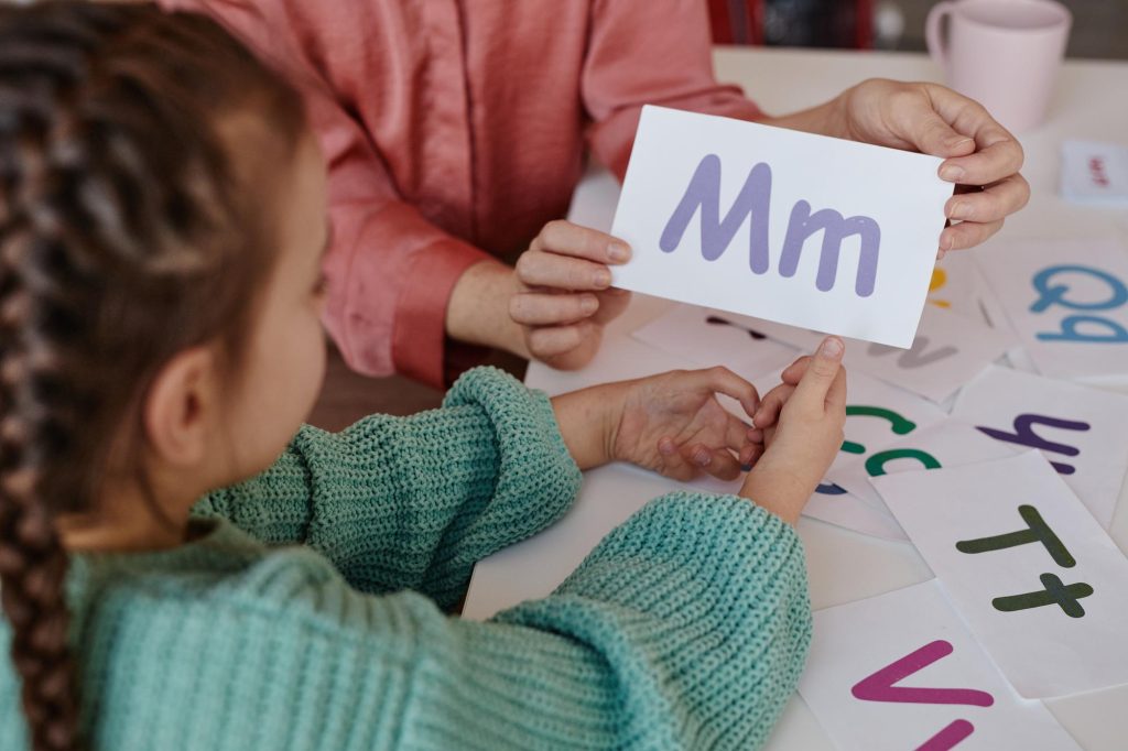 Une fillette et un adulte examinent une carte-lettre « Mm » lors d'une activité sur la dyslexie et la dysorthographie.