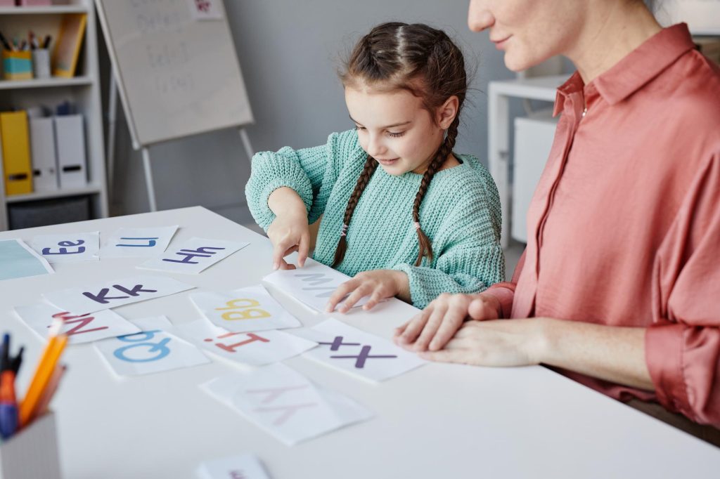 Enfant et adulte travaillant ensemble sur des cartes-lettres dans une activité pédagogique liée à la dyslexie et à la dysorthographie.