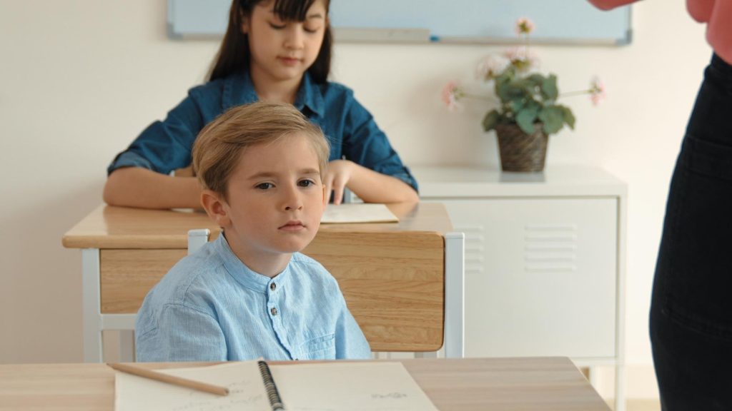 Jeune garçon soucieux à son pupitre, illustrant les signes de TDAH en classe. 