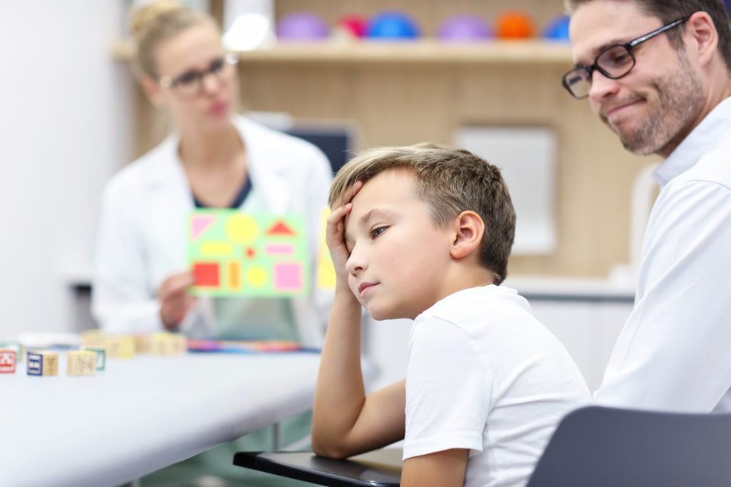 L'enfant se tient la tête pendant qu'une neuropsychologue présente des cartes d'évaluation colorées. 